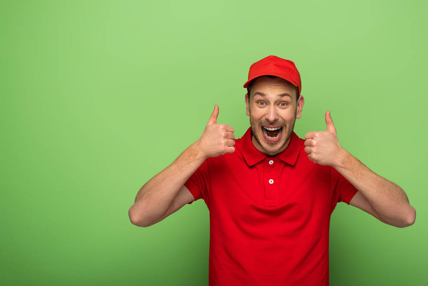 Aufgeregter Zusteller in roter Uniform zeigt Daumen hoch auf Grün - Foto, Bild