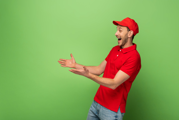 side view boldog futár piros egyenruhában nyitott karokkal zöld háttér - Fotó, kép