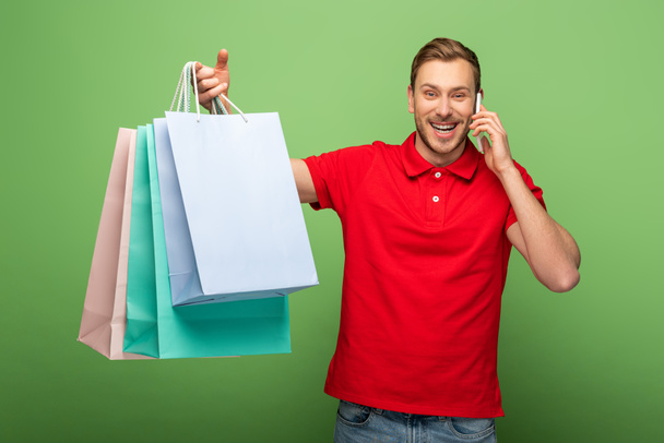 happy man holding shopping bags and talking on smartphone on green - Photo, Image