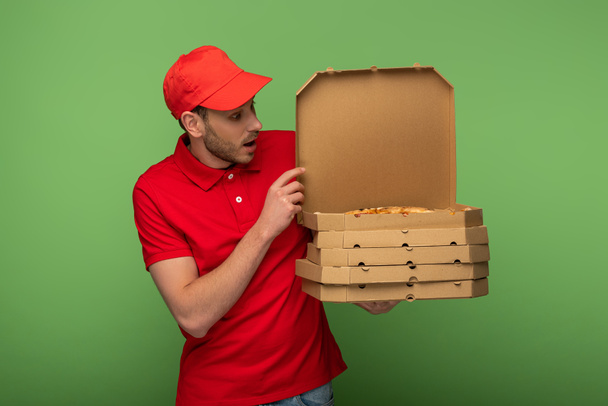 shocked delivery man in red uniform holding pizza boxes on green - Foto, afbeelding