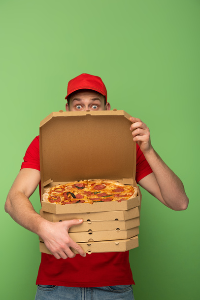 megdöbbent futár piros egyenruhában elbújik pizza dobozok mögött a zöldön - Fotó, kép