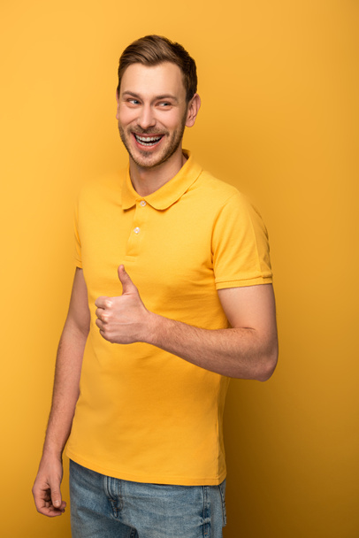 happy handsome man in yellow outfit showing thumb up on yellow background - 写真・画像