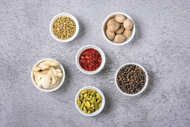 mix of aromatic spices coriander, black pepper, bergamot, dried ginger, nutmeg, paprika in white cups on gray concrete background Top view Flat lay Healthy food. - Photo, Image