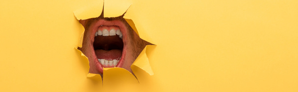 cropped view of open mouth in yellow paper hole  - Fotografie, Obrázek