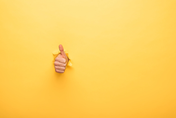 cropped view of man showing thumb up through yellow paper hole  - 写真・画像