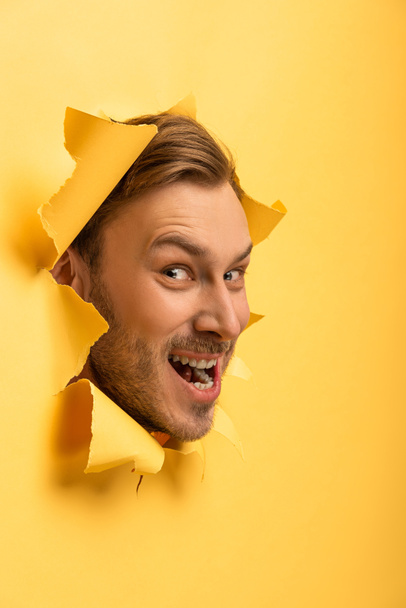 Τρελός όμορφος άντρας με κεφάλι σε κίτρινη χάρτινη τρύπα.  - Φωτογραφία, εικόνα