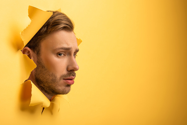 smutný pohledný muž s hlavou ve žluté papírové díře  - Fotografie, Obrázek