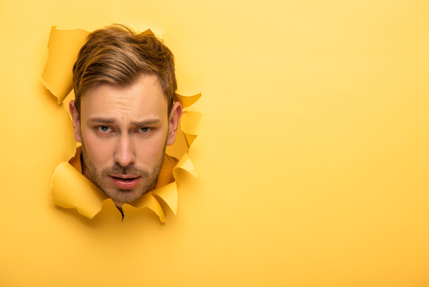 sad handsome man with head in yellow paper hole  - Foto, Bild