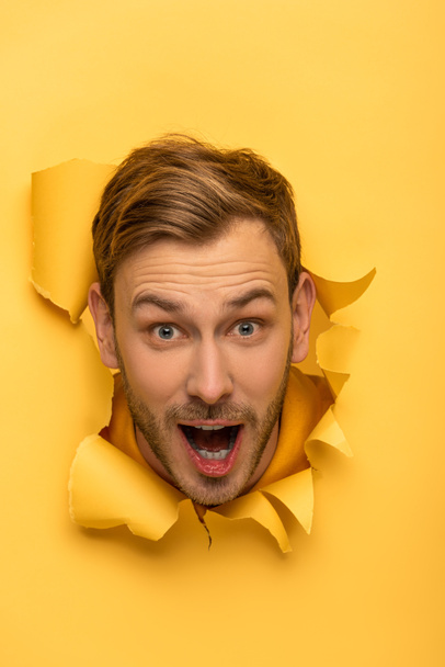 izgatott jóképű férfi fejjel sárga papír lyuk  - Fotó, kép
