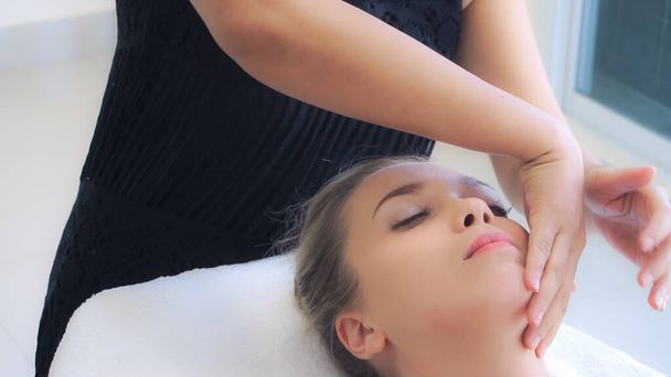 Расслабленная женщина лежит на спа-кровати для массажа лица и головы спа-процедуры массажистом в роскошном спа-курорте. Концепция оздоровления, снятия стресса и омоложения. - Фото, изображение