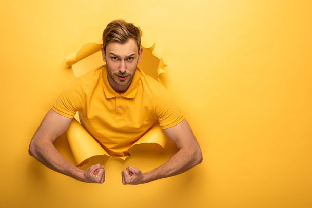 starker gutaussehender Mann im gelben Outfit mit Bizeps in gelbem Papierloch  - Foto, Bild