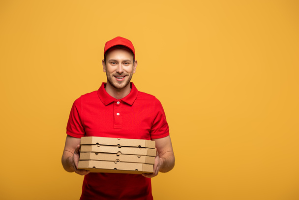 happy delivery man in red uniform holding pizza boxes isolated on yellow - Foto, Bild