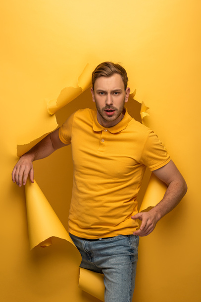 handsome man in yellow outfit walking through yellow paper hole  - Фото, зображення