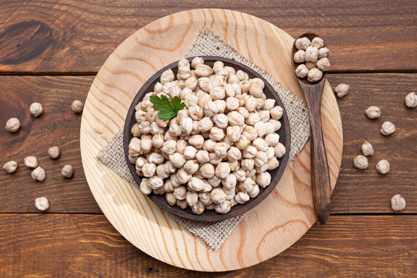 Chickpeas on a wooden plate, wooden spoon on a wooden base Top view.  - Photo, Image