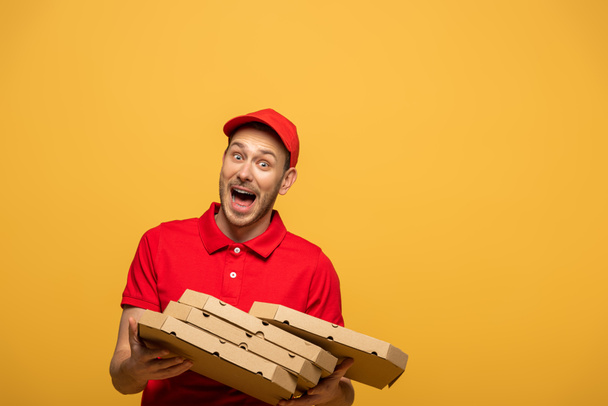 scared delivery man in red uniform dropping pizza boxes and screaming isolated on yellow - Фото, изображение
