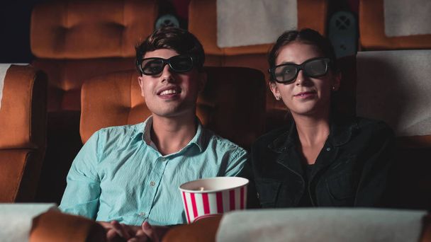 Man and woman in the cinema watching a movie with 3D glasses. with interest looking at the screen, exciting and eating popcorn - Photo, Image
