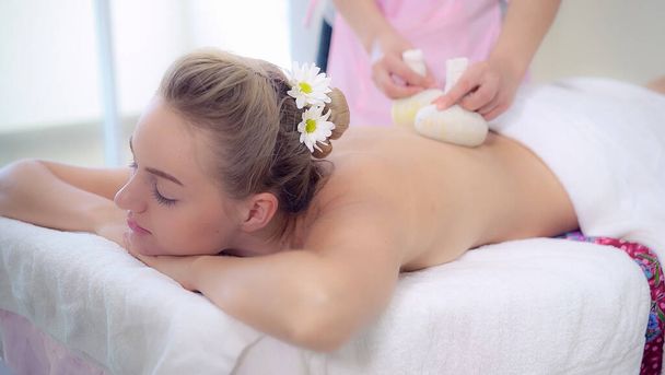 Massage therapist holds a herbal compress to do treatment to woman lying on spa bed in a luxury spa resort. Wellness, stress relief and rejuvenation concept. - Fotografie, Obrázek