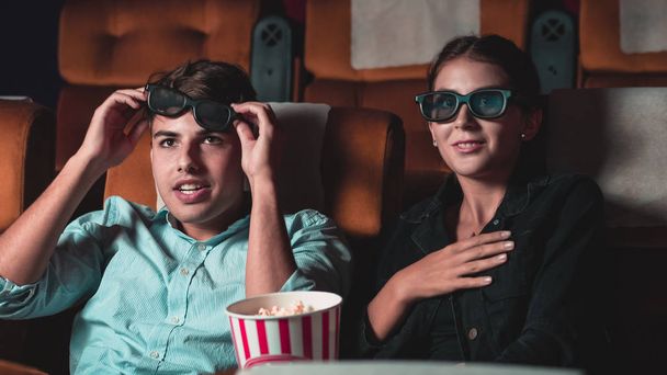 Мужчина и женщина в кино смотрят фильм в 3D очках. с интересом смотрит на экран, волнуется и ест кукурузу - Фото, изображение