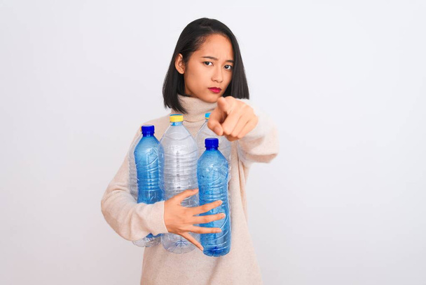 Nuori kaunis kiinalainen nainen kierrättää muovipulloja yli eristetty valkoinen tausta sormella kameraan ja sinulle, käsi merkki, positiivinen ja luottavainen ele edestä
 - Valokuva, kuva