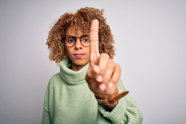 Joven mujer afroamericana hermosa con jersey de cuello alto y gafas Señalando con el dedo hacia arriba y la expresión enojada, mostrando ningún gesto
 - Foto, Imagen