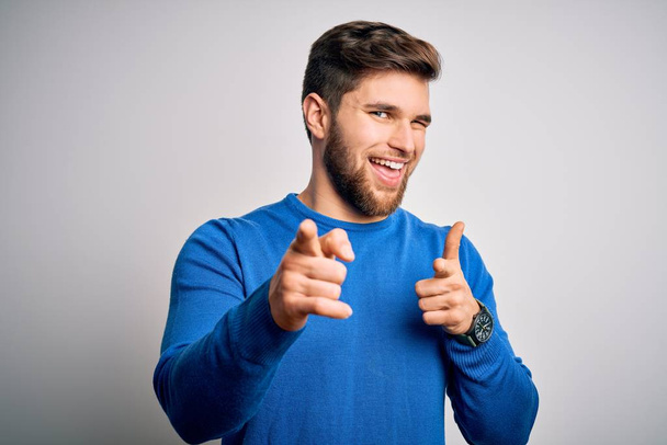 Young handsome blond man with beard and blue eyes wearing casual sweater pointing fingers to camera with happy and funny face. Good energy and vibes. - Photo, Image
