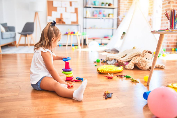 Jovem menina loira bonita que gosta de jogar escola com brinquedos no jardim de infância, sorrindo feliz jogando com brinquedos de inteligência em casa
 - Foto, Imagem