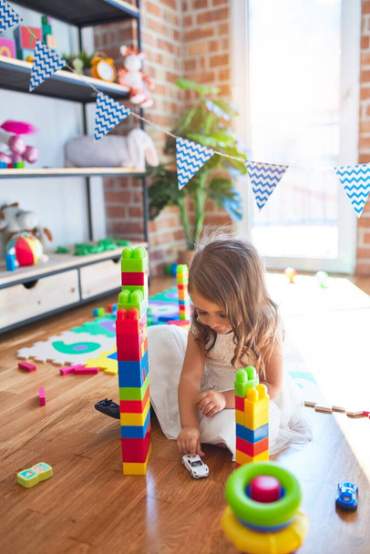 Adorabile bambino biondo che gioca con i blocchi di costruzione intorno a un sacco di giocattoli all'asilo
 - Foto, immagini