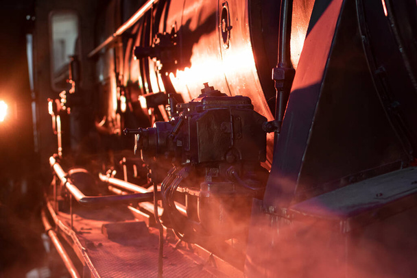 Dampfzug-Lokomotive nähert sich einem Bahnhof, der durch einen Güterbahnhof fährt und lässt von hinten Rauch und Dampf aufsteigen, was ein atmosphärisches Foto erzeugt - Foto, Bild
