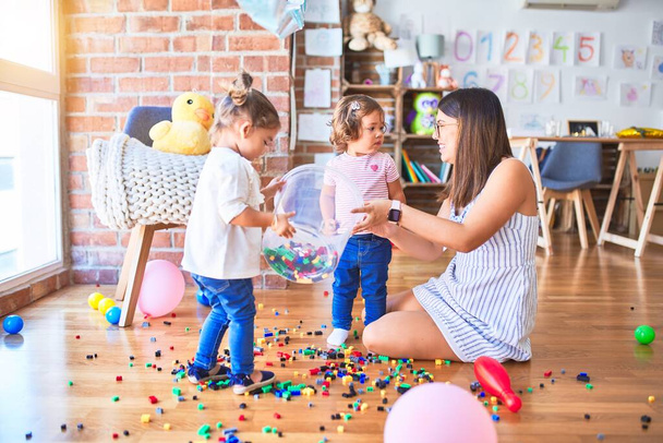 Joven hermosa maestra y niños pequeños jugando con bloques de construcción de juguete en el jardín de infantes
 - Foto, Imagen