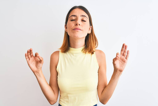 Belle femme rousse portant un t-shirt jaune d'été sur fond isolé se détendre et sourire les yeux fermés en faisant un geste de méditation avec les doigts. Concept de yoga
. - Photo, image