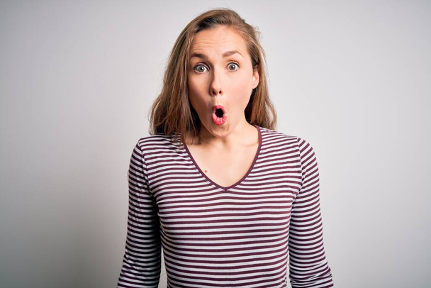 Young beautiful blonde woman wearing casual striped t-shirt over isolated white background afraid and shocked with surprise expression, fear and excited face. - Photo, Image
