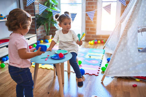 Adorables tout-petits jouant des repas en utilisant des aliments en plastique et des couverts jouet à la maternelle
 - Photo, image