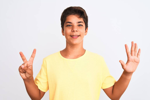 Jóképű tinédzser fiú áll a fehér elszigetelt háttér mutatja, és rámutatva ujjak száma 7 miközben mosolygós magabiztos és boldog. - Fotó, kép