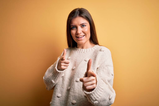 Young beautiful woman with blue eyes wearing casual sweater standing over yellow background pointing fingers to camera with happy and funny face. Good energy and vibes. - Fotó, kép