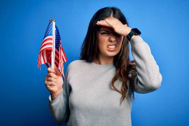 Young beautiful brunette patriotic woman holding american flag celebrating 4th of july stressed with hand on head, shocked with shame and surprise face, angry and frustrated. Fear and upset for mistake. - Foto, immagini