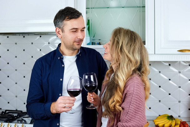 Paar hält Weingläser in der Küche und schaut einander an - Foto, Bild