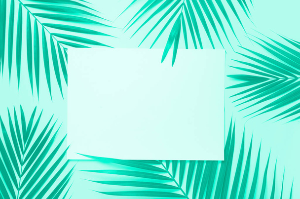 Tropical palm leaves on mint color background with paper card note. Minimal summer concept. Trendy green and turquoise color. Creative layout. Top view, flat lay. - Photo, Image