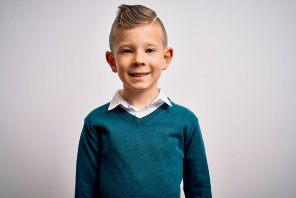 Νεαρό μικρό καυκάσιο παιδί με μπλε μάτια που στέκεται φορώντας κομψά ρούχα πάνω σε απομονωμένο φόντο με ένα χαρούμενο και δροσερό χαμόγελο στο πρόσωπο. Τυχερός άνθρωπος. - Φωτογραφία, εικόνα