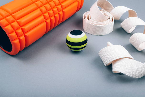 Set of green fascia release ball, orange bumpy foam massage roller for trigger points and belt over grey background. - Photo, Image