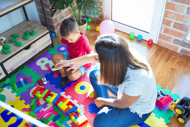 Giovane bella insegnante e bambino che gioca con blocchi di costruzione intorno a un sacco di giocattoli all'asilo
 - Foto, immagini