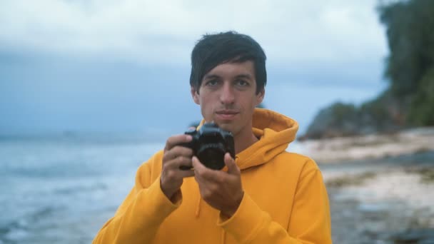 mężczyzna fotograf w żółtej bluzie robi zdjęcie na pięknej dzikiej tropikalnej plaży w godzinach wieczornych - Materiał filmowy, wideo