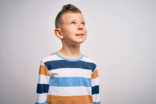 Jeune enfant caucasien aux yeux bleus portant une chemise rayée sur fond isolé regardant de côté avec le sourire sur le visage, expression naturelle. Rire confiant
. - Photo, image