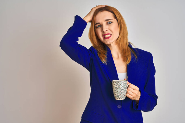 Redhead caucasian business woman drinking a cup of coffee over isolated background stressed with hand on head, shocked with shame and surprise face, angry and frustrated. Fear and upset for mistake. - Foto, afbeelding