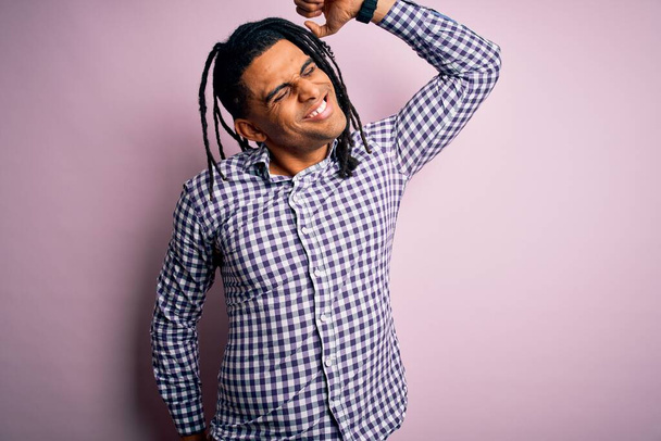 Νεαρός όμορφος Αφροαμερικάνος με κοτσιδάκια που φοράει casual πουκάμισο που τεντώνεται προς τα πίσω, κουρασμένος και χαλαρός, νυσταγμένος και χασμουριέται νωρίς το πρωί - Φωτογραφία, εικόνα