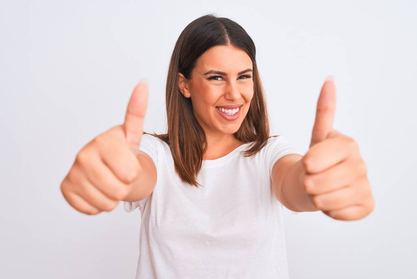 Portrait of beautiful and young brunette woman standing over isolated white background approving doing positive gesture with hand, thumbs up smiling and happy for success. Winner gesture. - Photo, Image