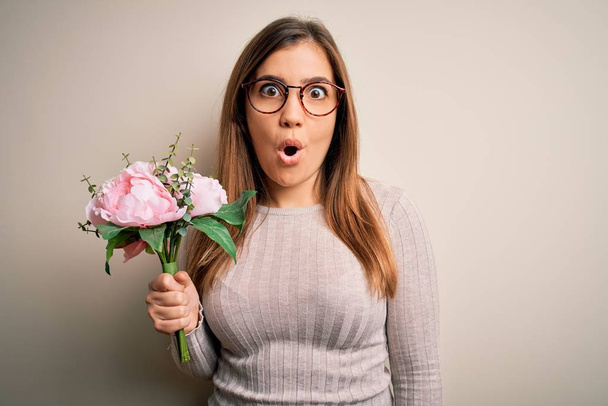 Young blonde woman holding beautiful romantic floral bouquet over isolated background scared in shock with a surprise face, afraid and excited with fear expression - Photo, Image