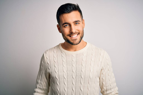Junger gutaussehender Mann in lässigem Pullover, der vor isoliertem weißem Hintergrund steht, mit einem fröhlichen und kühlen Lächeln im Gesicht. Glücklicher Mensch. - Foto, Bild