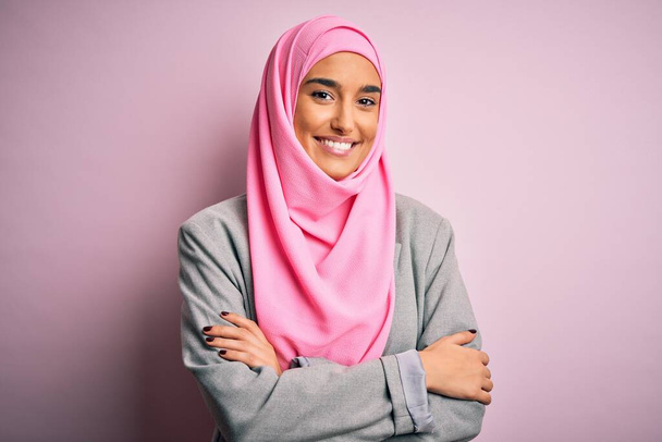 Fiatal gyönyörű barna üzletasszony rózsaszín muszlim hidzsábot és üzleti dzsekit visel boldog arc mosolyogva keresztbe tett karokkal nézi a kamerát. Pozitív személy. - Fotó, kép