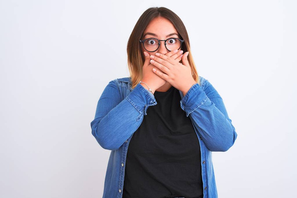Young beautiful woman wearing denim shirt and glasses over isolated white background shocked covering mouth with hands for mistake. Secret concept. - Foto, Bild