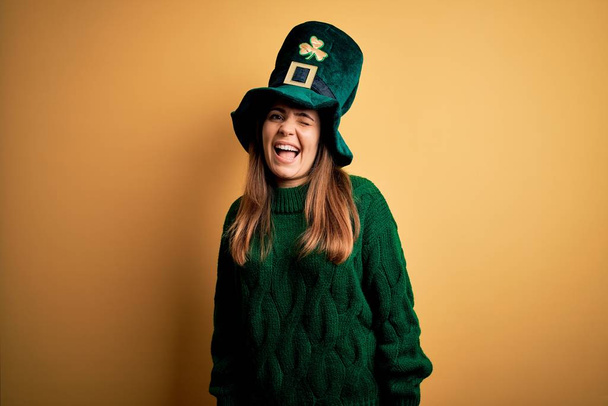 Νεαρή όμορφη μελαχρινή γυναίκα φορώντας πράσινο καπέλο στον εορτασμό του Αγίου Πατρικίου να κλείνει το μάτι κοιτάζοντας την κάμερα με σέξι έκφραση, χαρούμενο και χαρούμενο πρόσωπο. - Φωτογραφία, εικόνα